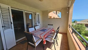A balcony with a table and chairs, a sliding glass door, and a view of the sea.