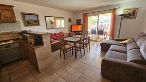 A living room with a sofa, dining table, chairs, a TV, and a kitchen area with a microwave.