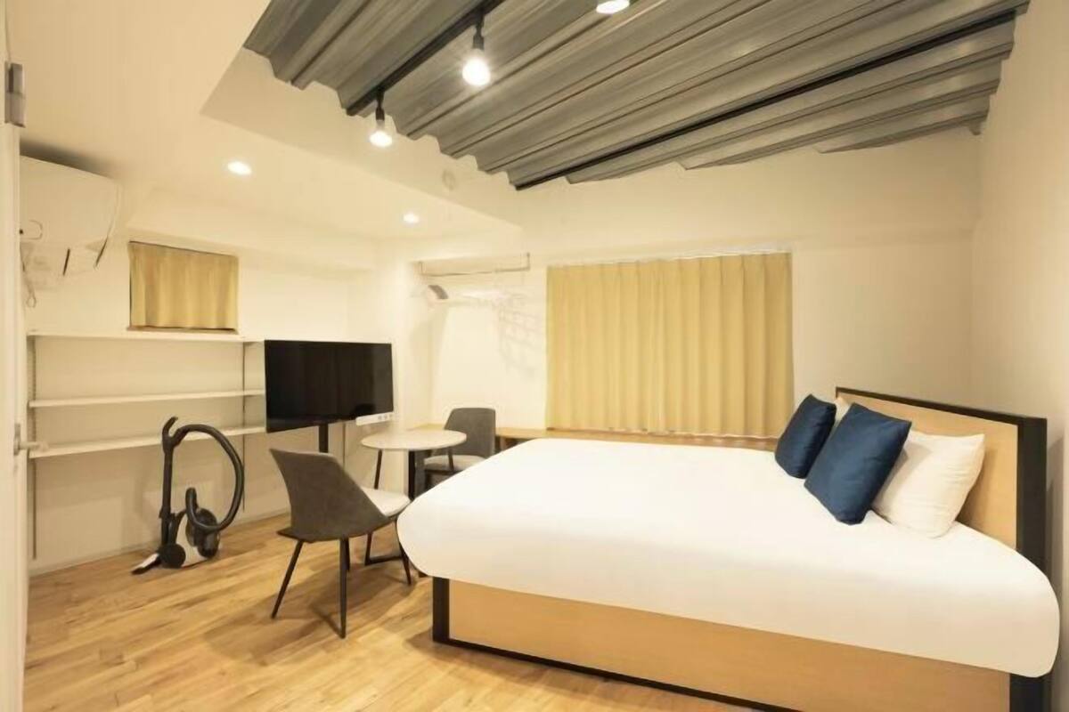 A modern hotel room with a bed, a desk, a chair, a TV, and a window with curtains.