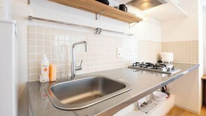 A modern kitchen with a stainless steel sink, white tiled backsplash, and a gas stove. - Gran FusionIkebukuro (Tokyo)