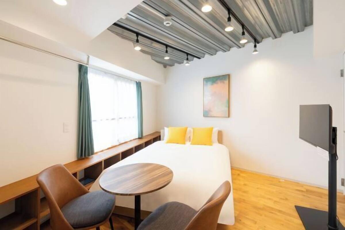 A hotel room with a bed, two chairs, a small table, a TV, and a painting on the wall.