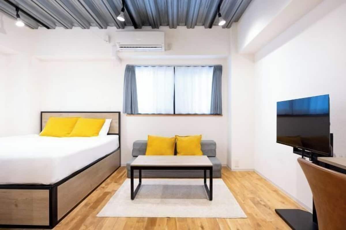 A modern hotel room with a bed, sofa, coffee table, TV, and an air conditioning unit.