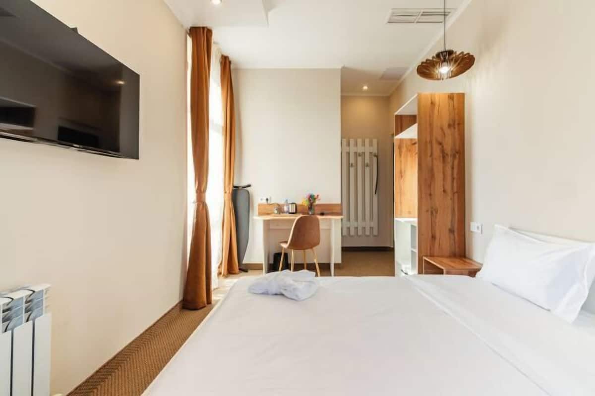 A hotel room with a bed, a desk, a chair, a TV, and a wooden accent wall.