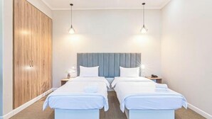 A hotel room with two beds, a wooden wardrobe, and pendant lights. - Aykun Hotel (Almaty)