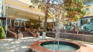 A courtyard with a circular fountain, a staircase, and a building with large windows. - Aykun Hotel (Almaty)