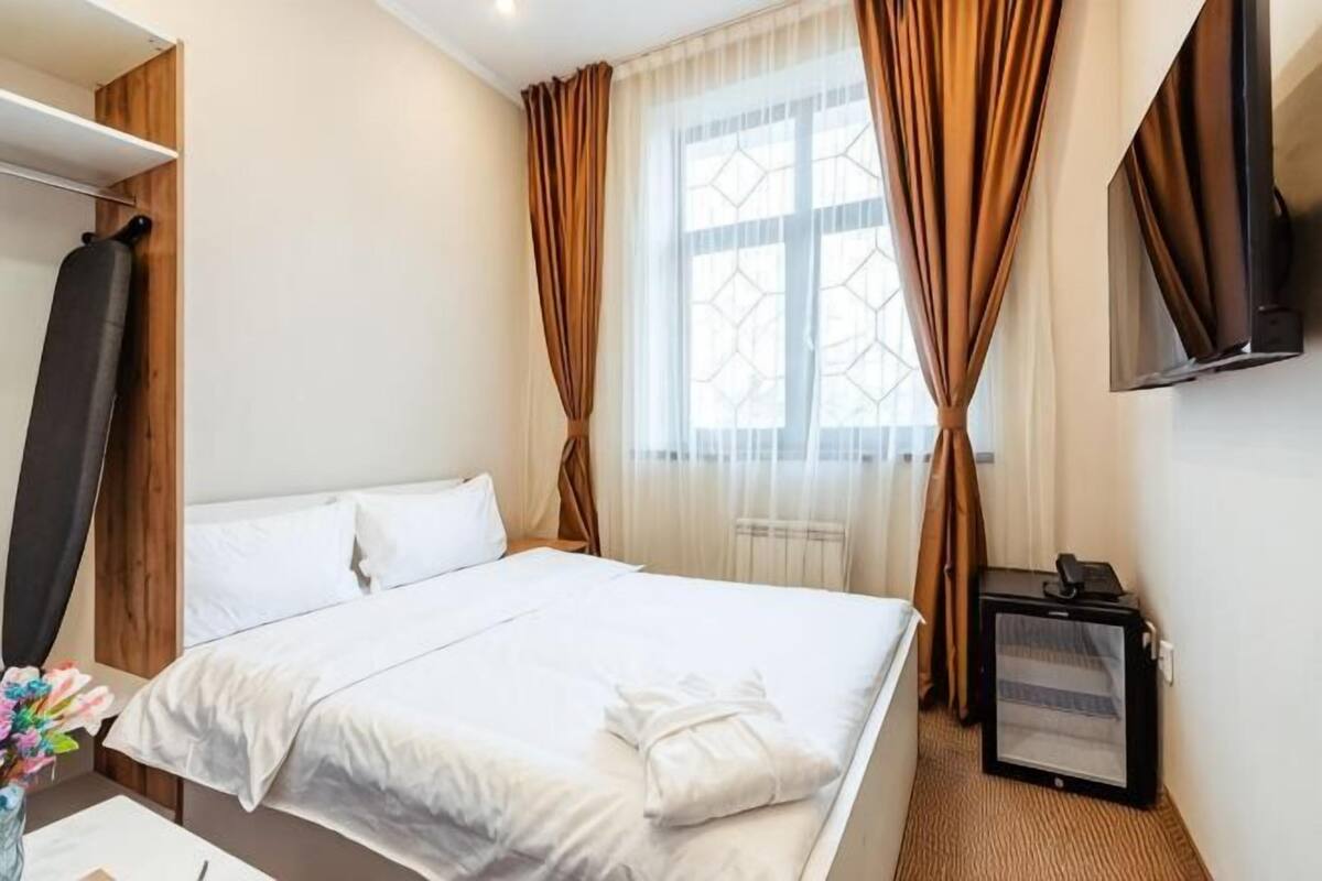 A hotel room with a bed, a TV, a window with curtains, and a desk with a computer.