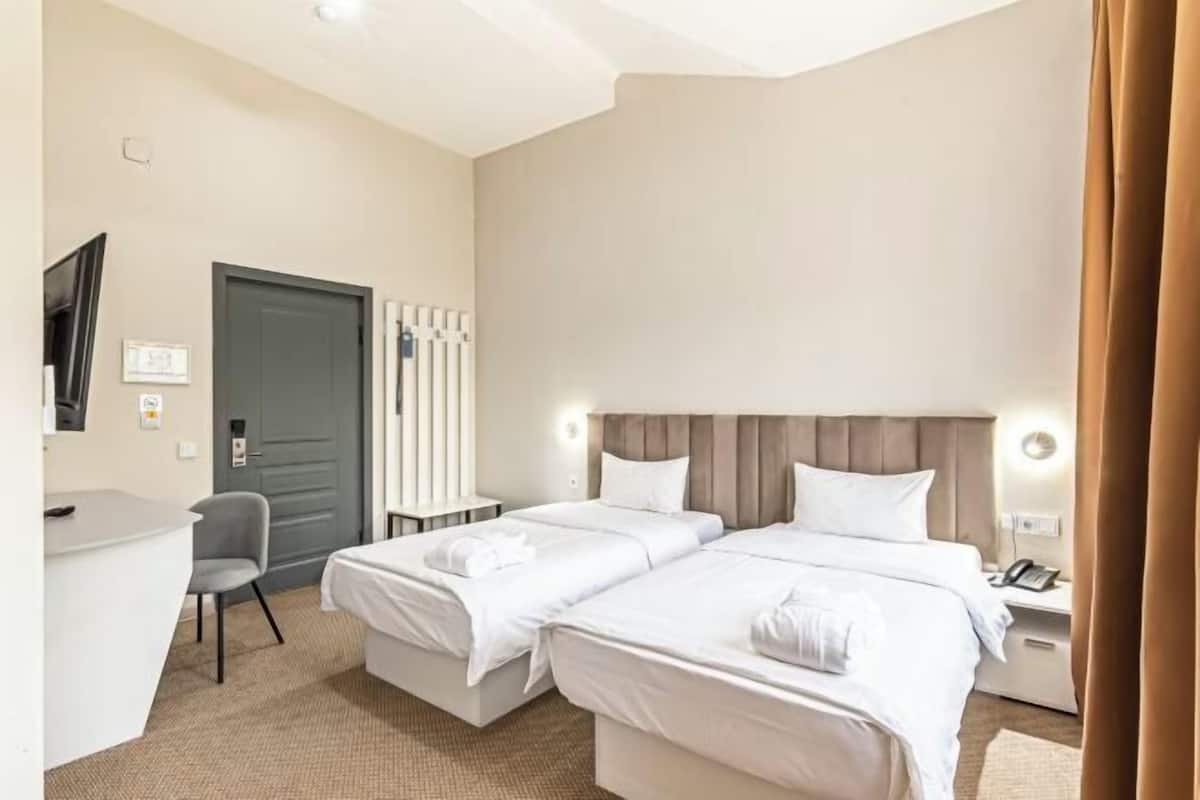 A hotel room with two beds, a desk, a chair, a door, and a nightstand with a phone.