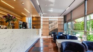 A modern hotel lobby with a marble reception desk, blue upholstered seating, and a staircase leading to upper floors. - Aykun Hotel (Almaty)