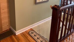 A staircase with a wooden handrail, a framed botanical print on the wall, a smoke detector, and a doormat. - Cozy Ranch Retreat Near Jefferson City - Fun Games, Activities, Sports, & Land! (Loose Creek)