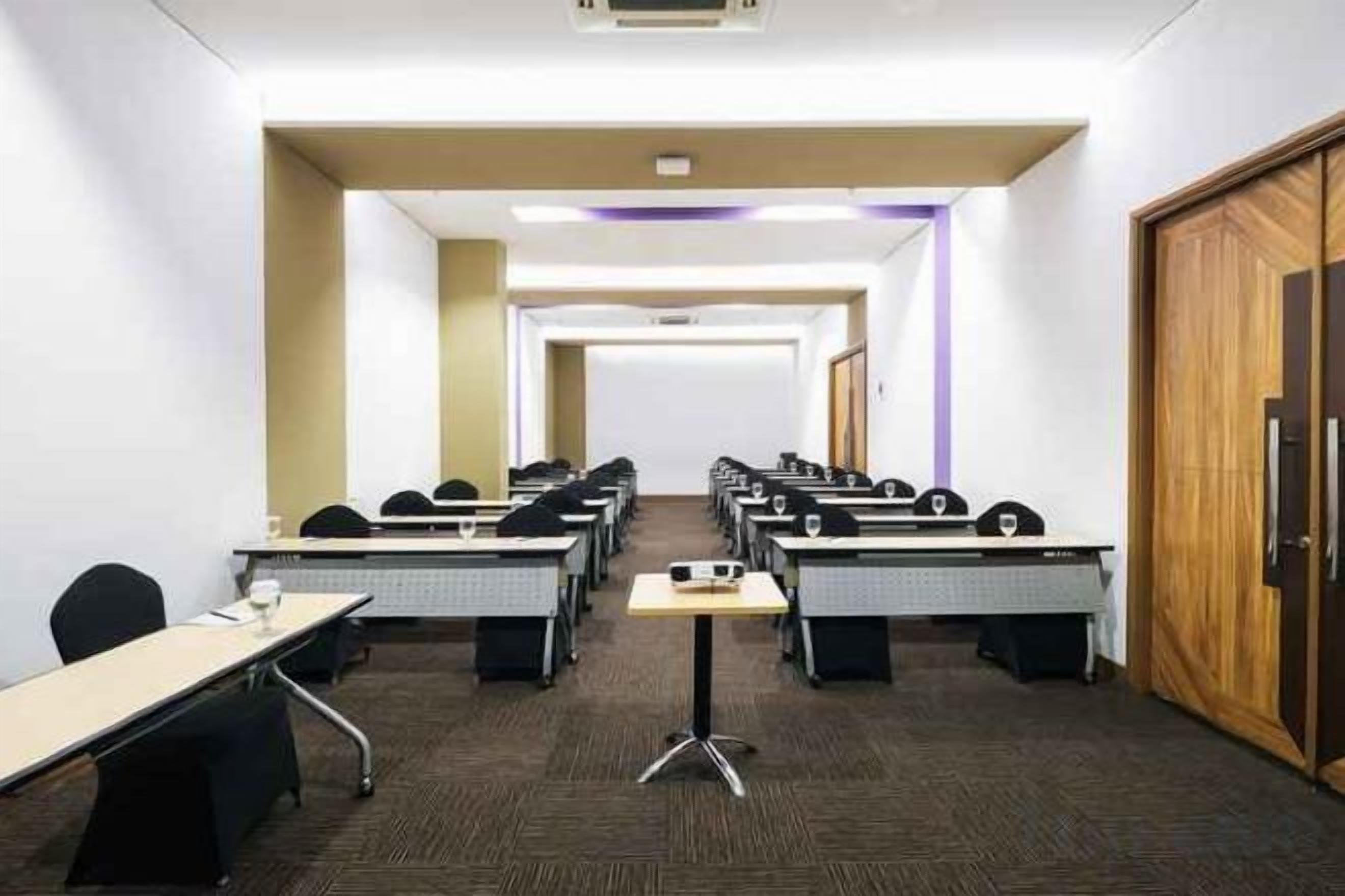 A conference room with rows of tables and chairs, a wooden door, and a carpeted floor.