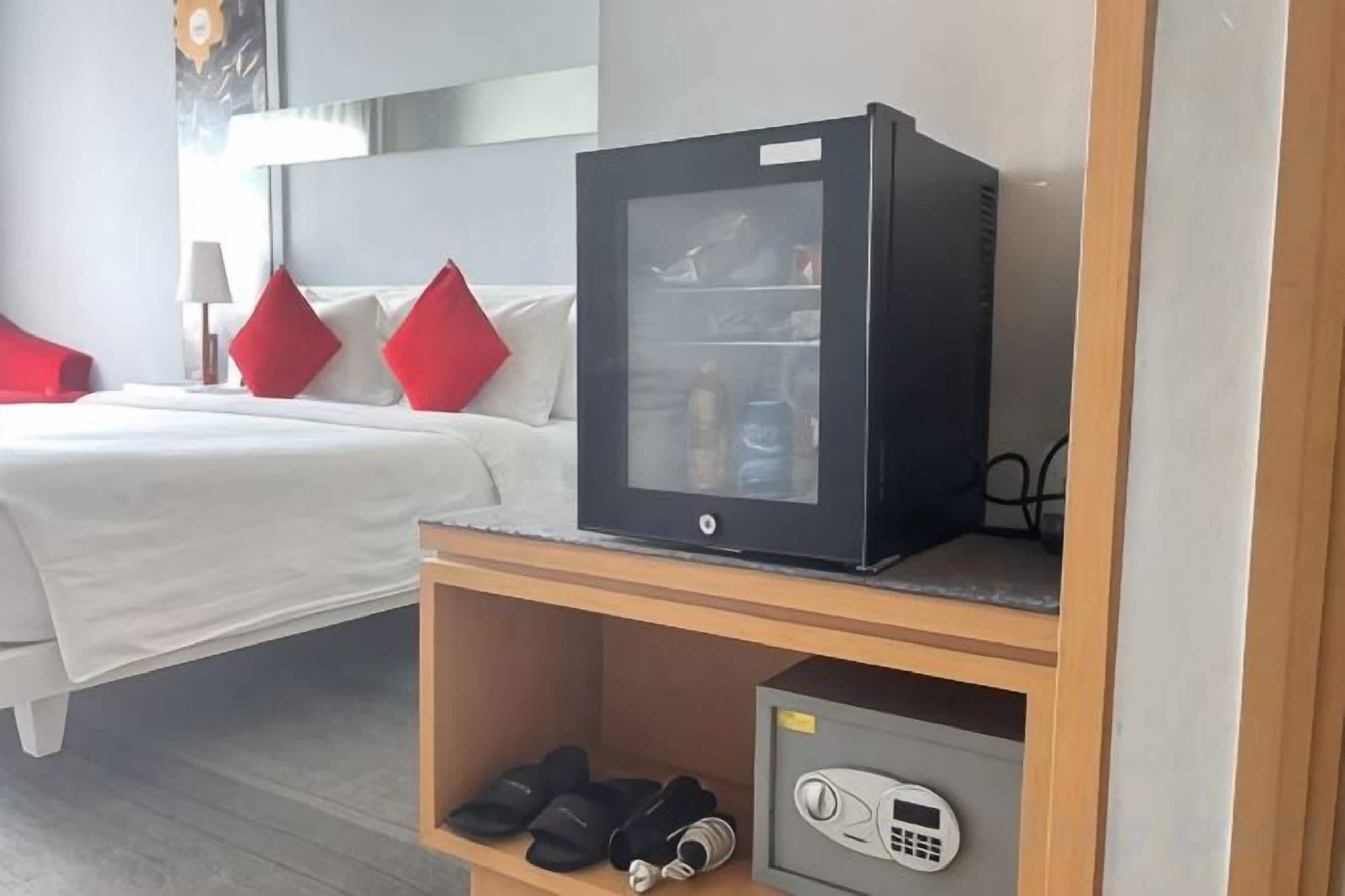 A hotel room with a bed, a minibar, a television, and a shoe rack.