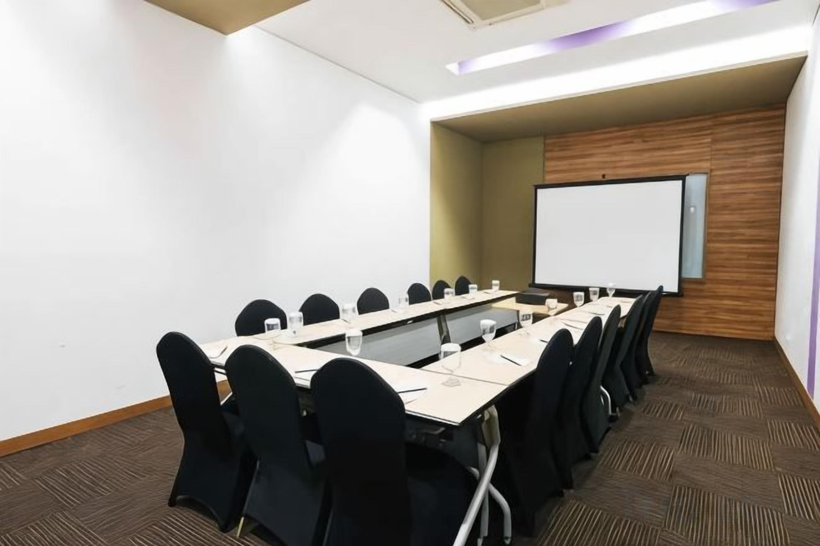 Ein Konferenzraum mit einem langen Tisch, Stühlen, einer Projektionsleinwand und einer Whiteboard-Tafel.