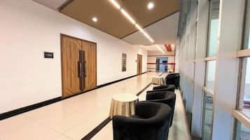 A hotel corridor with a row of black armchairs, a wooden door, and a small round table.