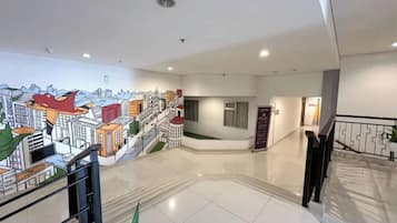 A hotel lobby with a modern design, featuring a large mural, a staircase, and a reception desk.