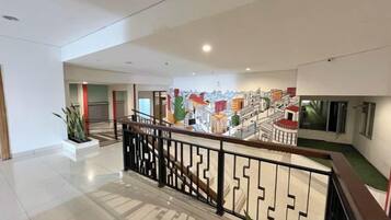 A modern hotel lobby with a staircase, a mural, and a plant.