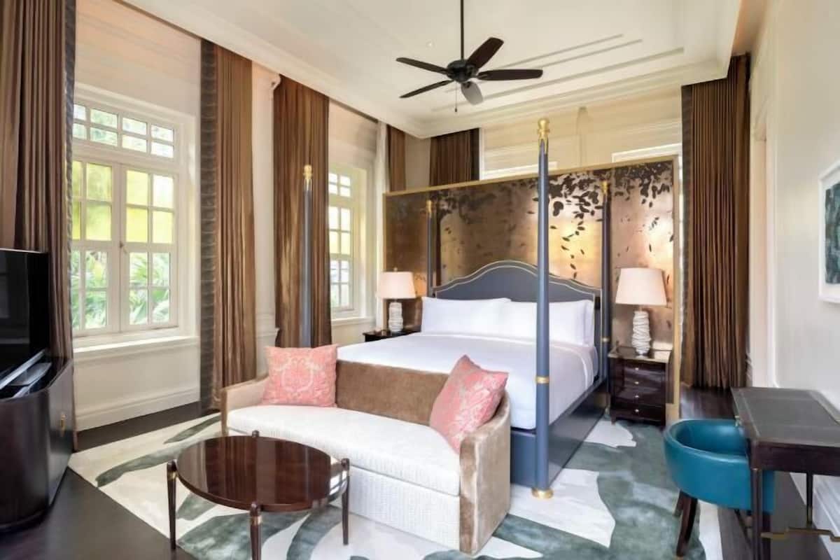 A hotel room with a four-poster bed, a sofa, a TV, and a desk.