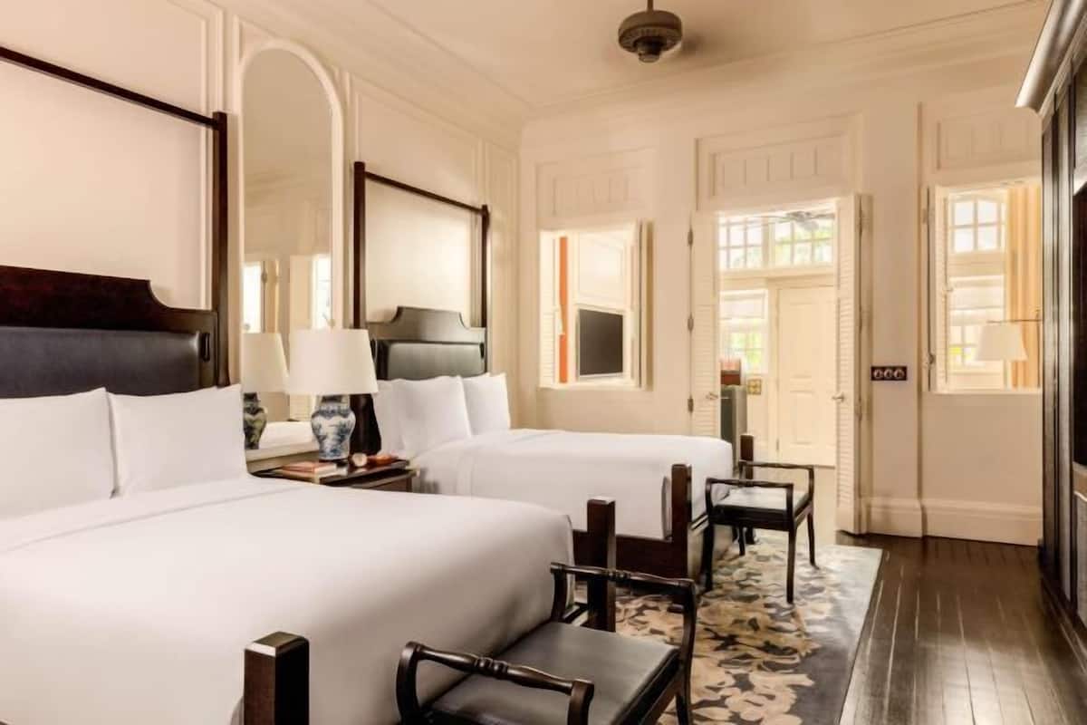 A hotel room with two beds, a large mirror, a wooden headboard, a nightstand with a lamp, and a floral-patterned rug.