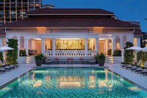 A poolside area with a tiled pool, lounge chairs, and a building with a tiled roof and columns. - Raffles Singapore (Singapore)