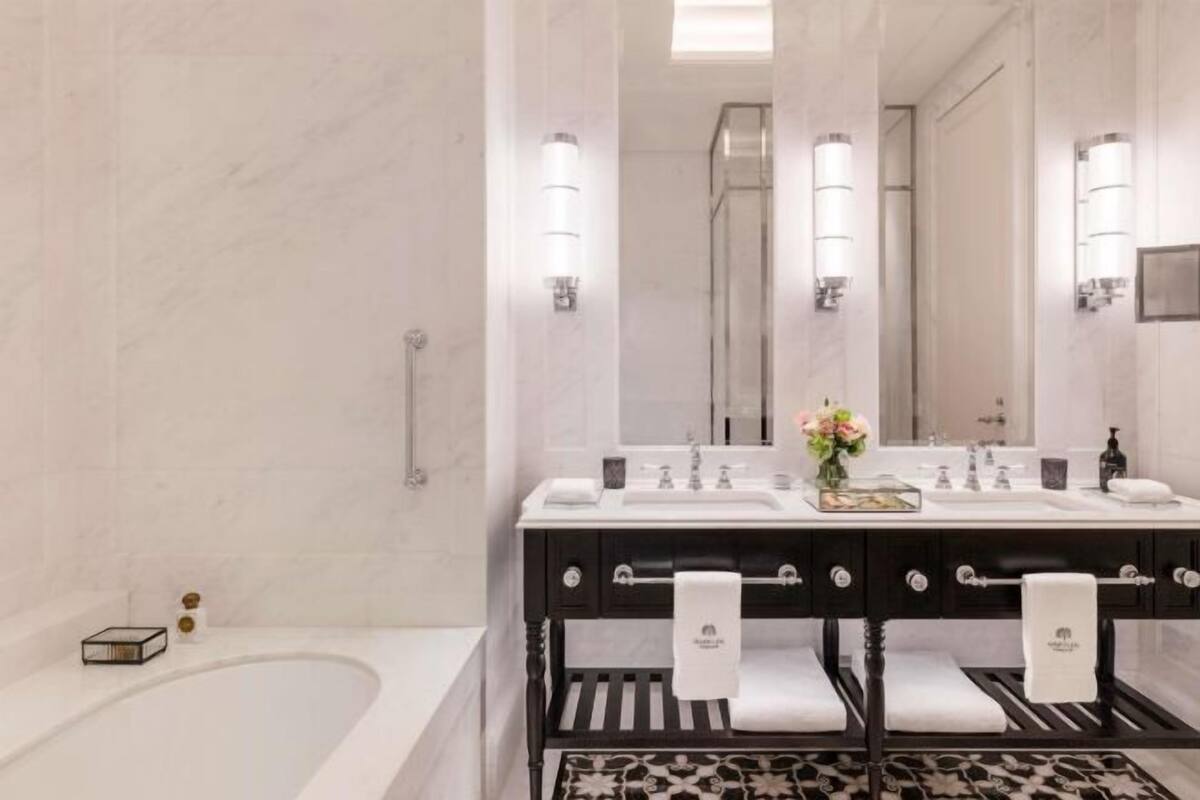 A modern bathroom with a freestanding bathtub, two sinks with black and white fixtures, and a large mirror above the vanity.