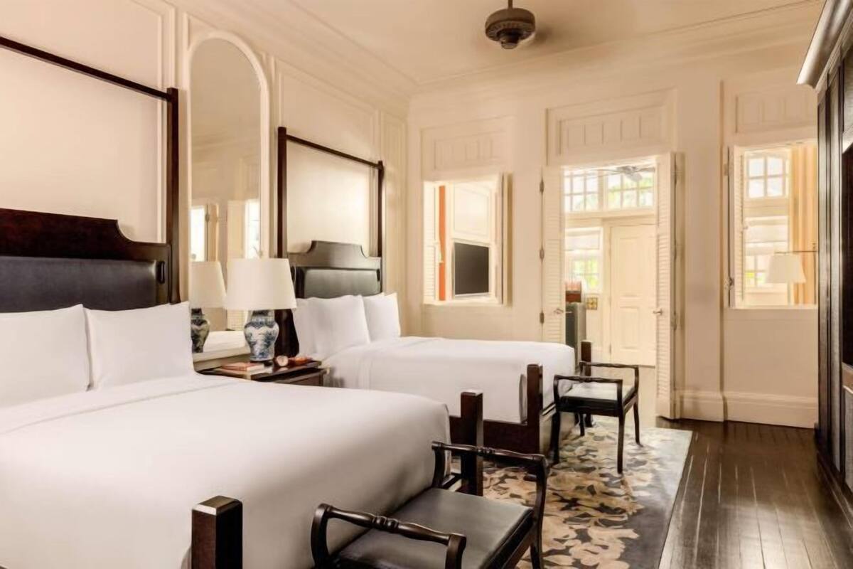A hotel room with two beds, a large mirror, a wooden headboard, a nightstand with a lamp, and a floral-patterned rug.