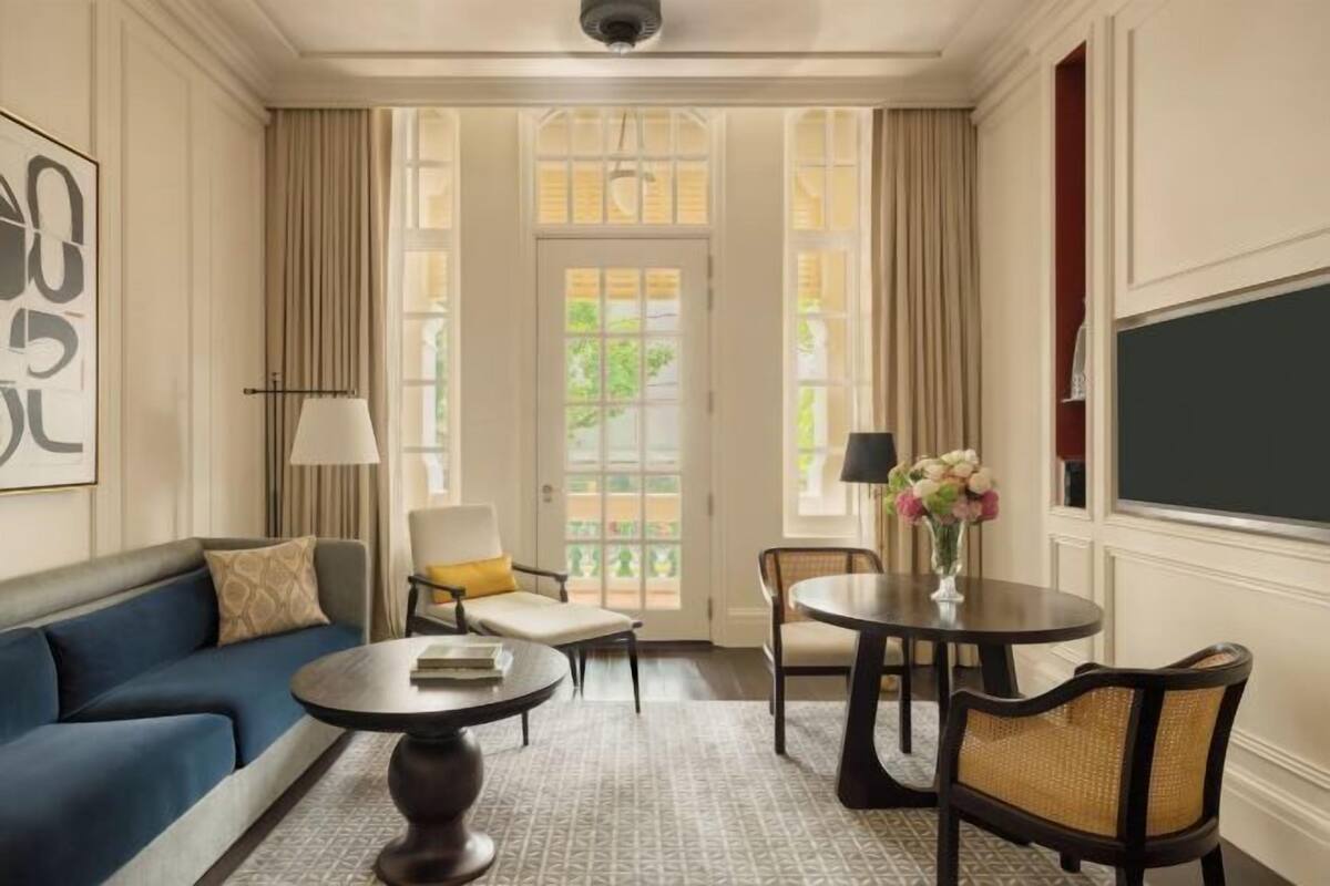 A room with a blue sofa, a round coffee table, a small table with a vase of flowers, and a chair.
