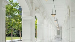 A white corridor with columns and hanging lamps, leading to a building entrance. - Raffles Singapore (Singapore)