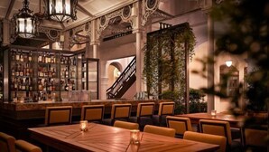 A bar area with a variety of liquor bottles, a staircase, and a seating area with tables and chairs. - Raffles Singapore (Singapore)
