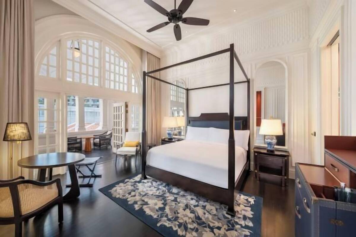 A four-poster bed in a hotel room with a large window, a round table, and a chair.