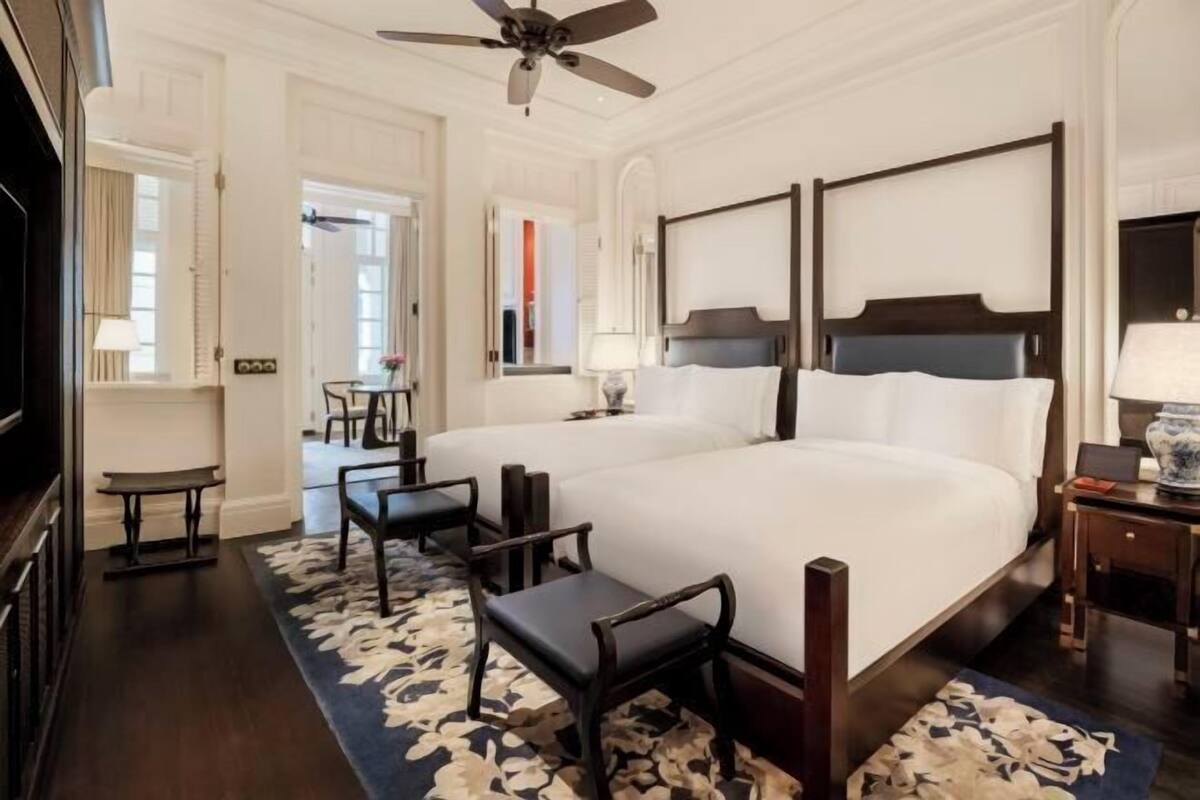 A hotel room with two large beds, a ceiling fan, a small table, and a chair.