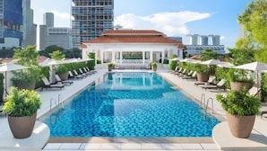 A swimming pool with lounge chairs and umbrellas, surrounded by potted plants. - Raffles Singapore (Singapore)
