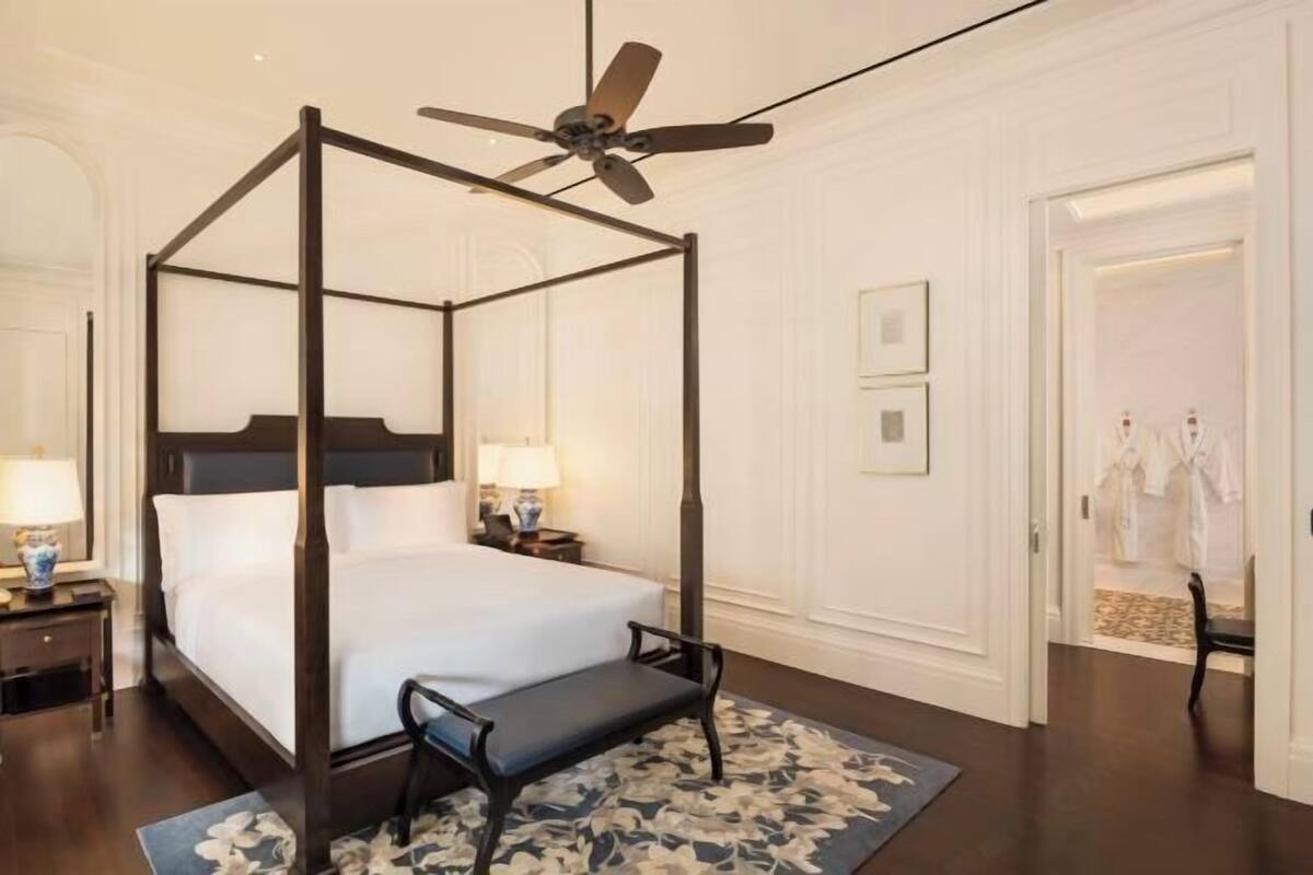 A four-poster bed with a ceiling fan, a bench, and a floral rug in a hotel room.