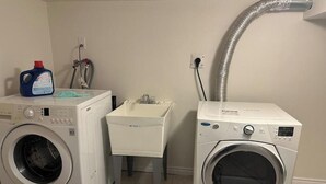 A laundry room with two front-loading washing machines, a white sink, and a hose connected to a wall outlet. - Ajax City Suite (Ajax)