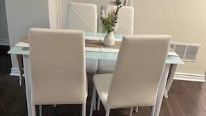 A dining area with a white table and chairs, a small white vase with a plant, and a white door in the background. - Ajax City Suite (Ajax)