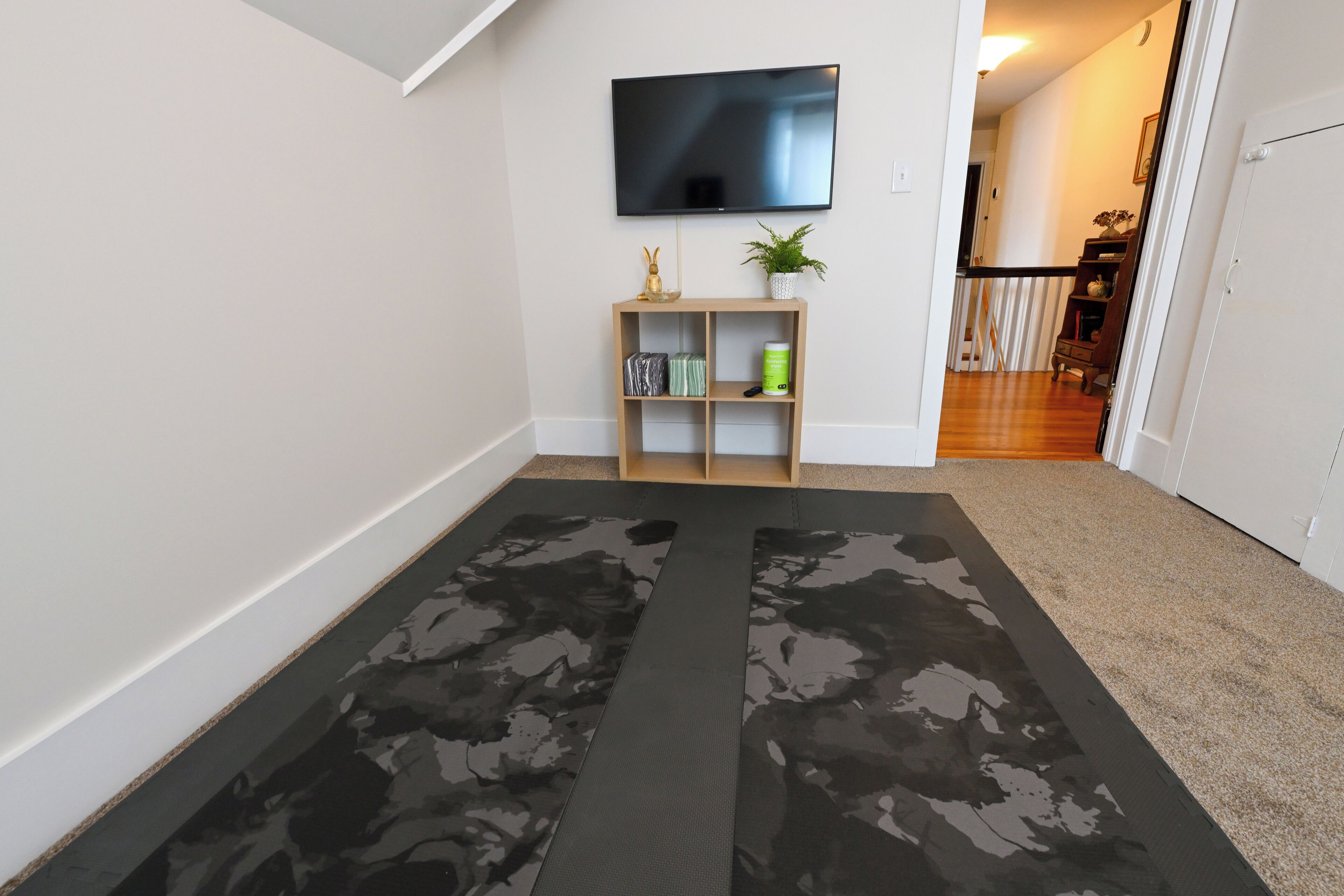 Un pasillo con un televisor de pantalla plana montado en la pared, un estante de madera con adornos y una alfombra estampada en el suelo.
