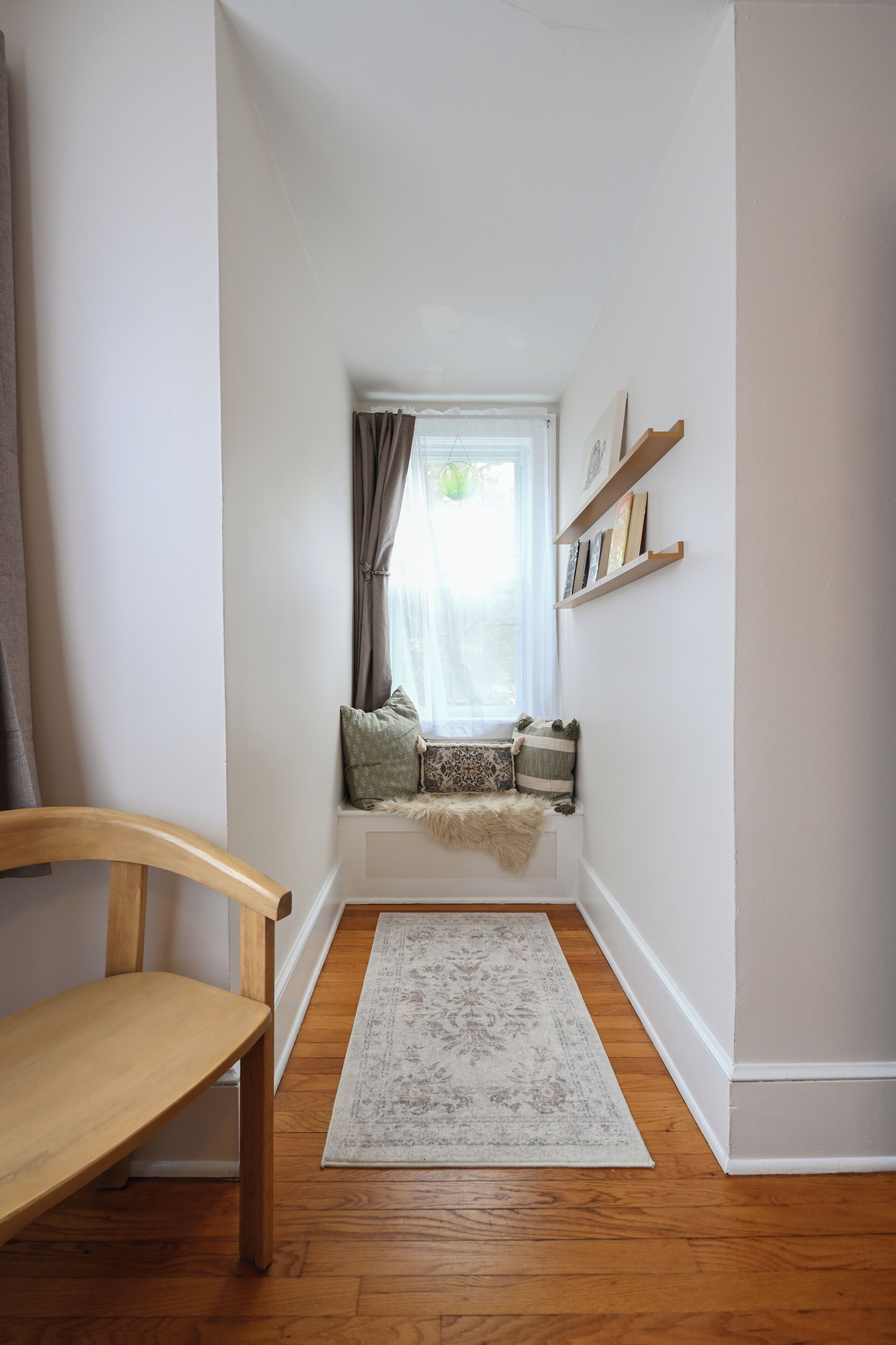 A narrow hallway with a wooden bench, a window with curtains, and a rug on the floor.