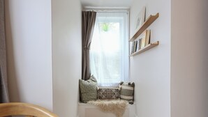Un pasillo estrecho con un banco de madera, una ventana con cortinas y una alfombra en el suelo.