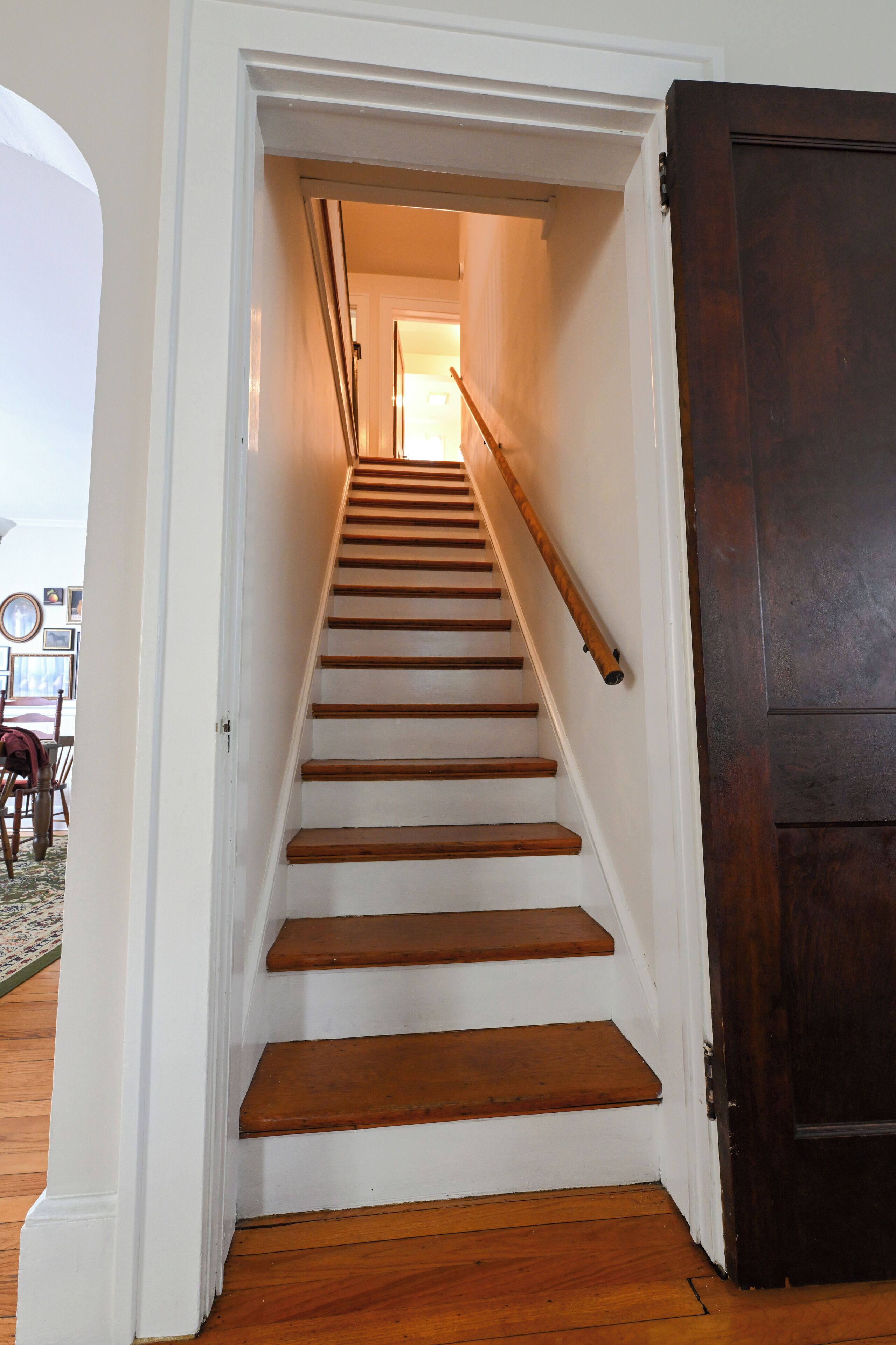 A wooden staircase with white walls and a dark door at the bottom.