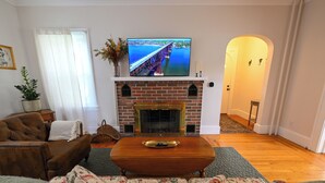 Una sala de estar con chimenea de ladrillo, un televisor montado encima y un sillón de cuero marrón.