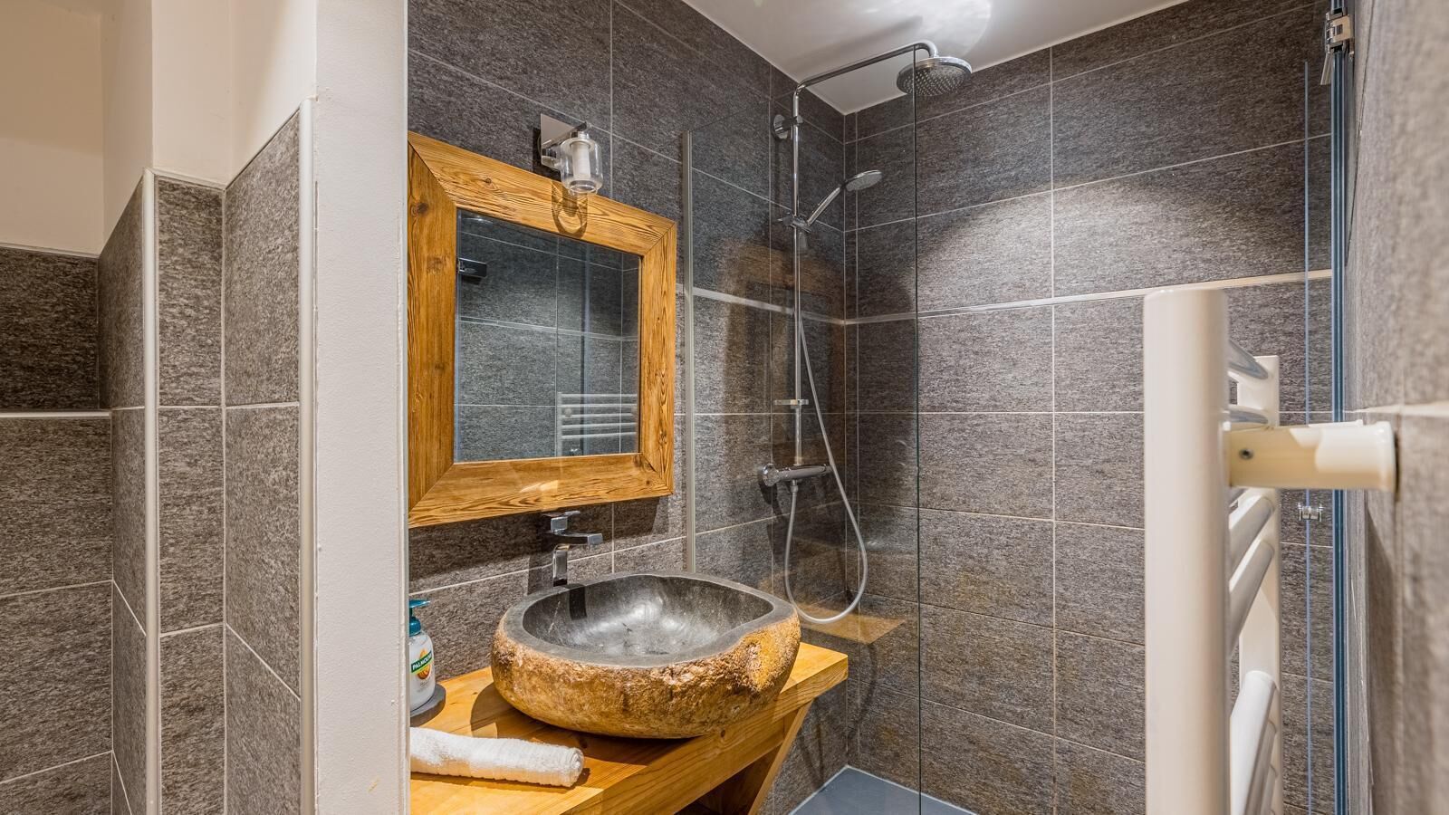 Ein Badezimmer mit einem Steintonnenwaschbecken, einem spiegelnden Wandbild mit Holzrahmen und einer Duschkabine.
