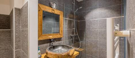 Ein Badezimmer mit einem Steintonnenwaschbecken, einem spiegelnden Wandbild mit Holzrahmen und einer Duschkabine.