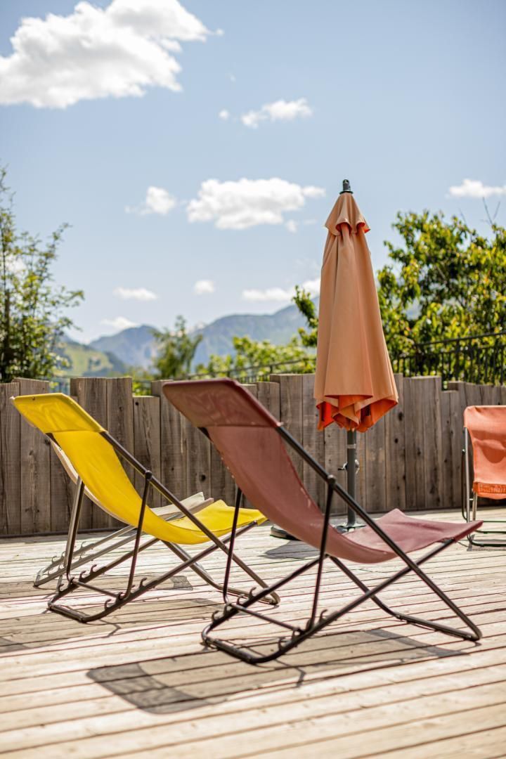 Een houten terras met twee opklapbare stoelen en één parasol.