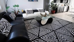 Ett modernt vardagsrum med en svartvit mönstrad matta, ett soffbord i glas och en svart lädersoffa med kuddar i zebraströmmigt mönster.