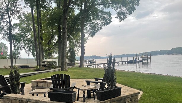 A patio area with outdoor furniture, a stone fire pit, and a view of a lake with boats.