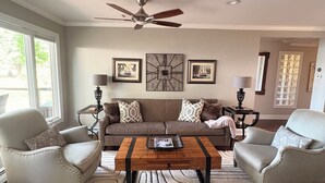 A living room with a sofa, two armchairs, a coffee table, a ceiling fan, and framed pictures on the wall.