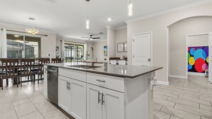 A modern kitchen with white cabinetry, a large island, and pendant lighting. - 6BR Disney Retreat w/ Pool, Game Loft & Resort Amenities (Kissimmee)