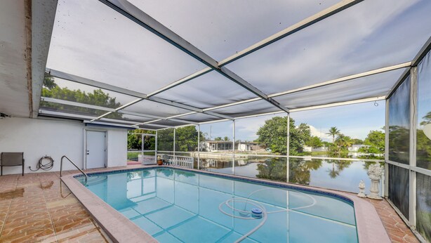 An indoor swimming pool with a clear view of the surrounding landscape, including trees and a body of water. - Canal-front Stay w/ Shared Pool, Near Hard Rock! (Miramar)