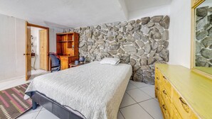 A bedroom with a stone wall, a bed with a patterned bedspread, a wooden dresser, and a desk with a chair. - Canal-front Stay w/ Shared Pool, Near Hard Rock! (Miramar)