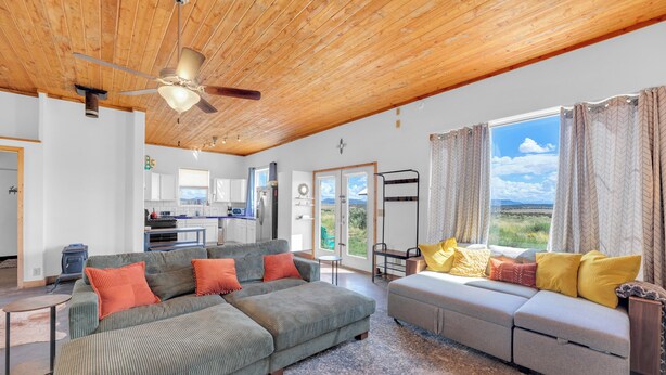 A spacious living area with a wooden ceiling, a large sofa with colorful cushions, a smaller sofa, and a view of the outdoors through a glass door. - Starry Sky + Serene Setting: Rural New Mexico Gem (Carrizozo)