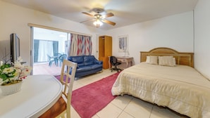 Une chambre à coucher comprenant un lit, un bureau, une chaise, un canapé, un ventilateur de plafond et une porte donnant sur un balcon.