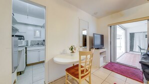 Un espace de vie compact comprenant un coin cuisine, un espace repas avec une table et une chaise, un téléviseur et une porte-fenêtre coulissante donnant sur un espace extérieur.